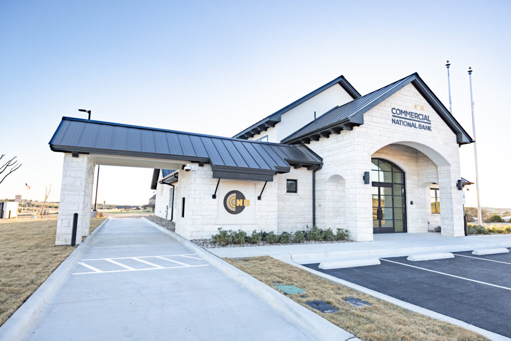 Angled exterior view of Commercial National Bank showing the drive-through canopy, stone facade, and front parking area in Burnet, TX.