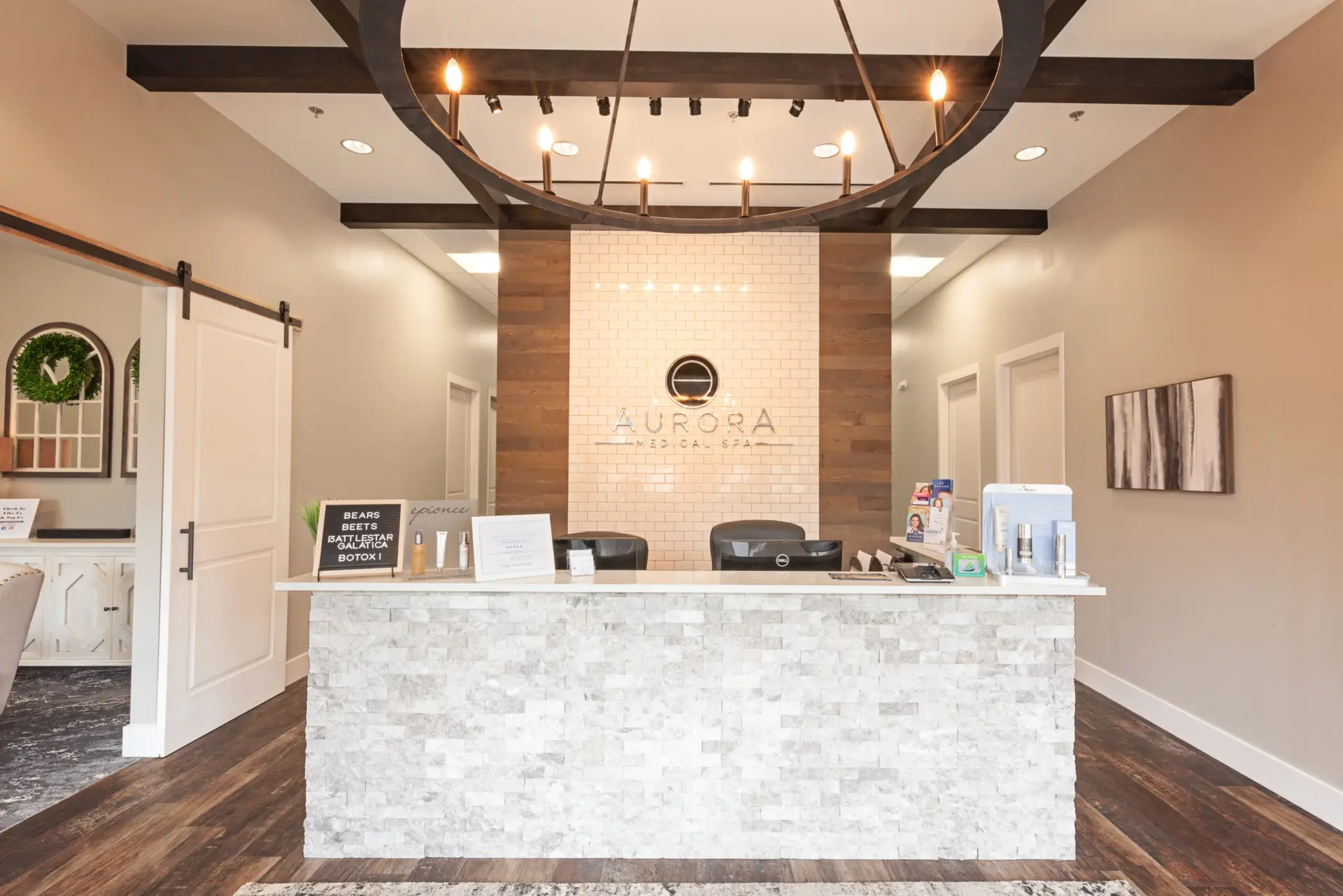 Aurora Med Spa reception area remodel in Georgetown TX by Synergy Commercial Construction featuring stone front desk, wood beam ceiling, and modern chandelier lighting