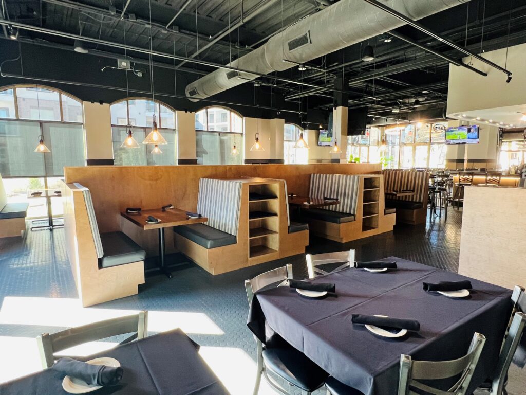 Remodeled restaurant dining room with booth seating, black table settings, wood accents, arched windows, and exposed ceiling details.