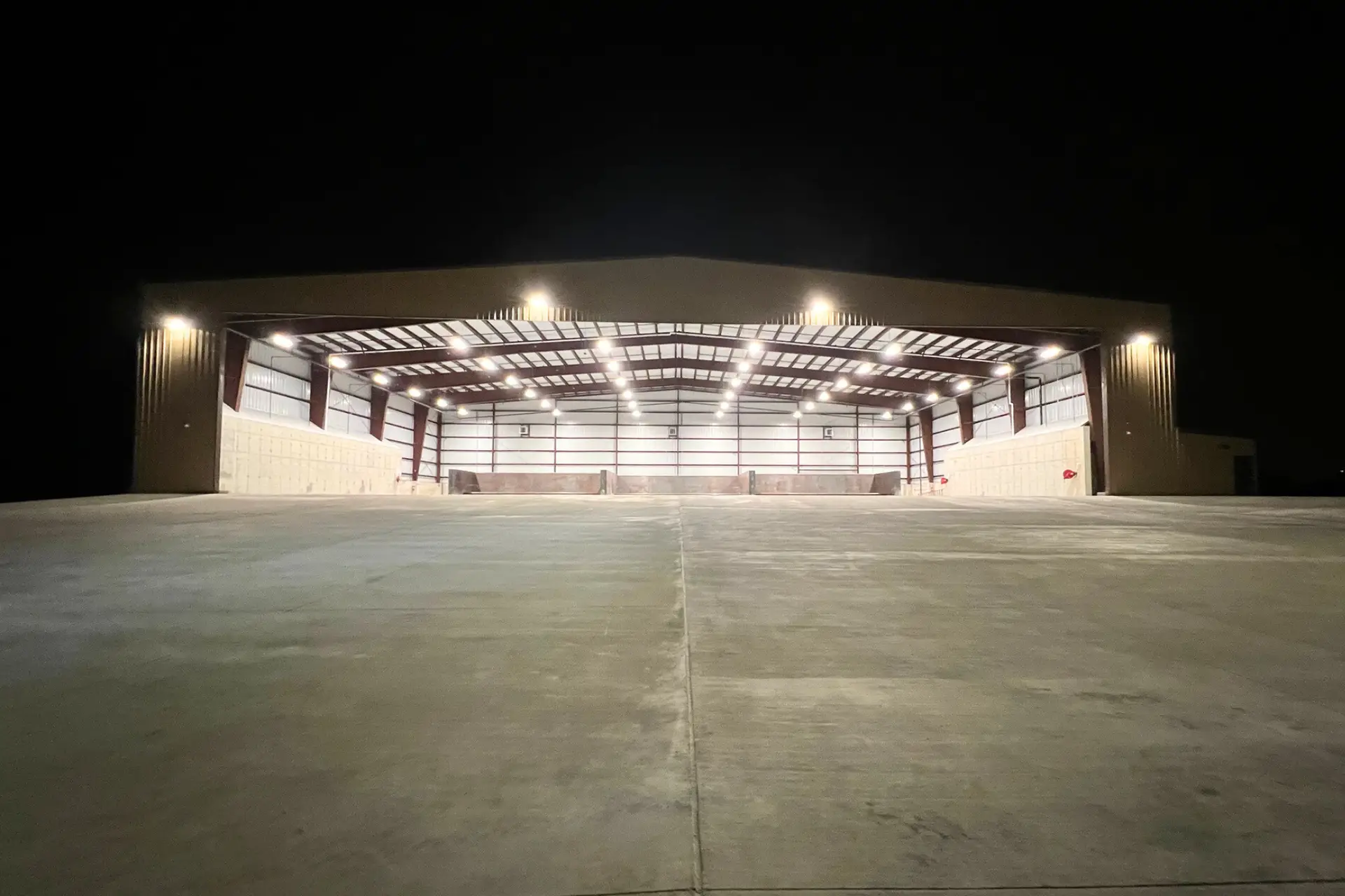 Nighttime exterior view of the transfer station loading building with large open bays and illuminated concrete work areas.