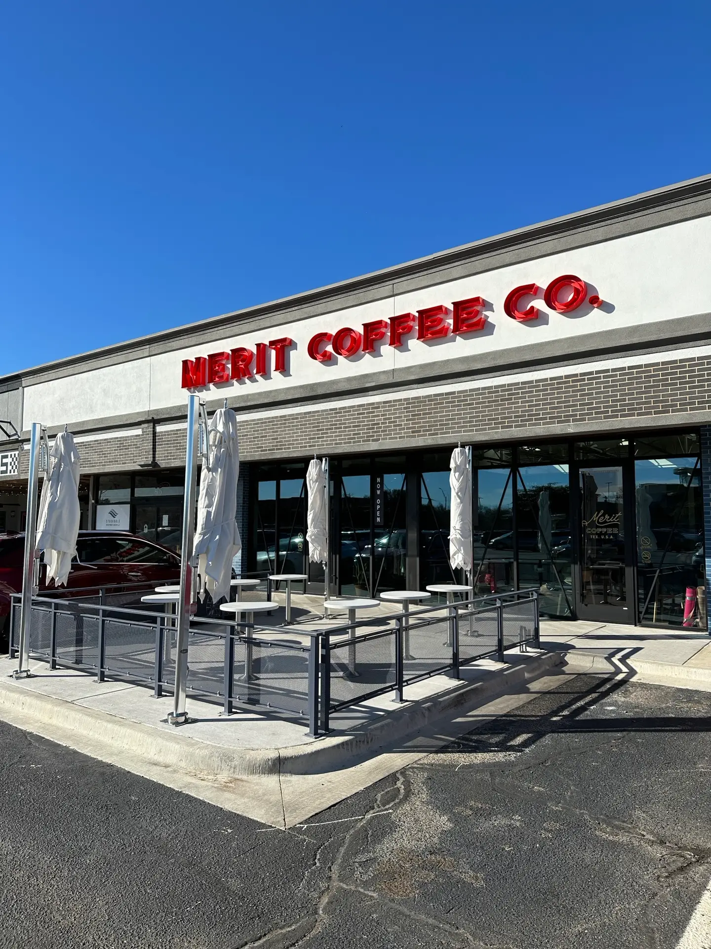 Merit Coffee storefront with outdoor patio seating, metal railings, and branded signage at a retail center in Dallas.