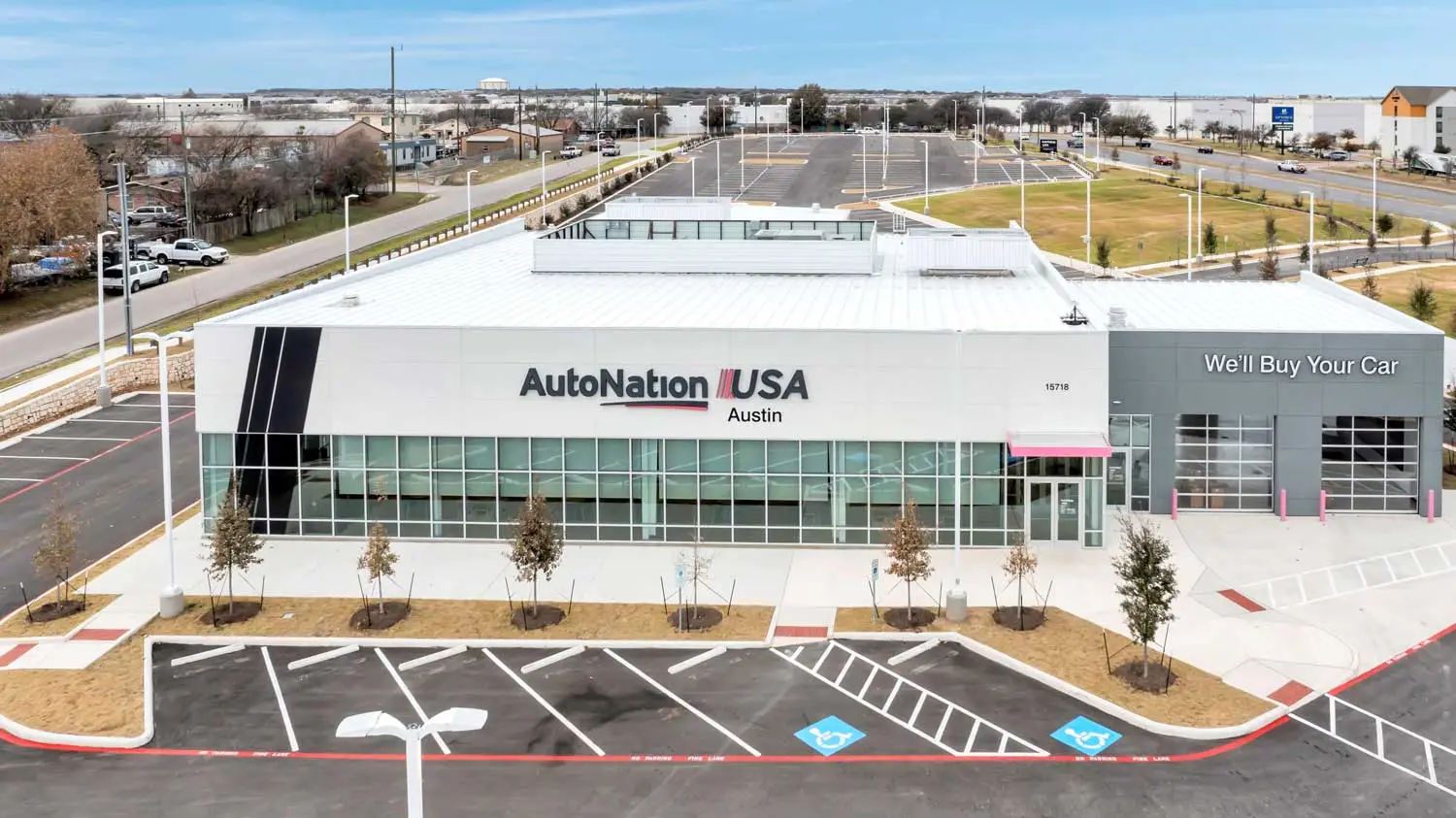 Front exterior of the AutoNation USA Austin dealership featuring glass storefront systems, vehicle service access, and customer parking areas constructed by Synergy Commercial Construction.