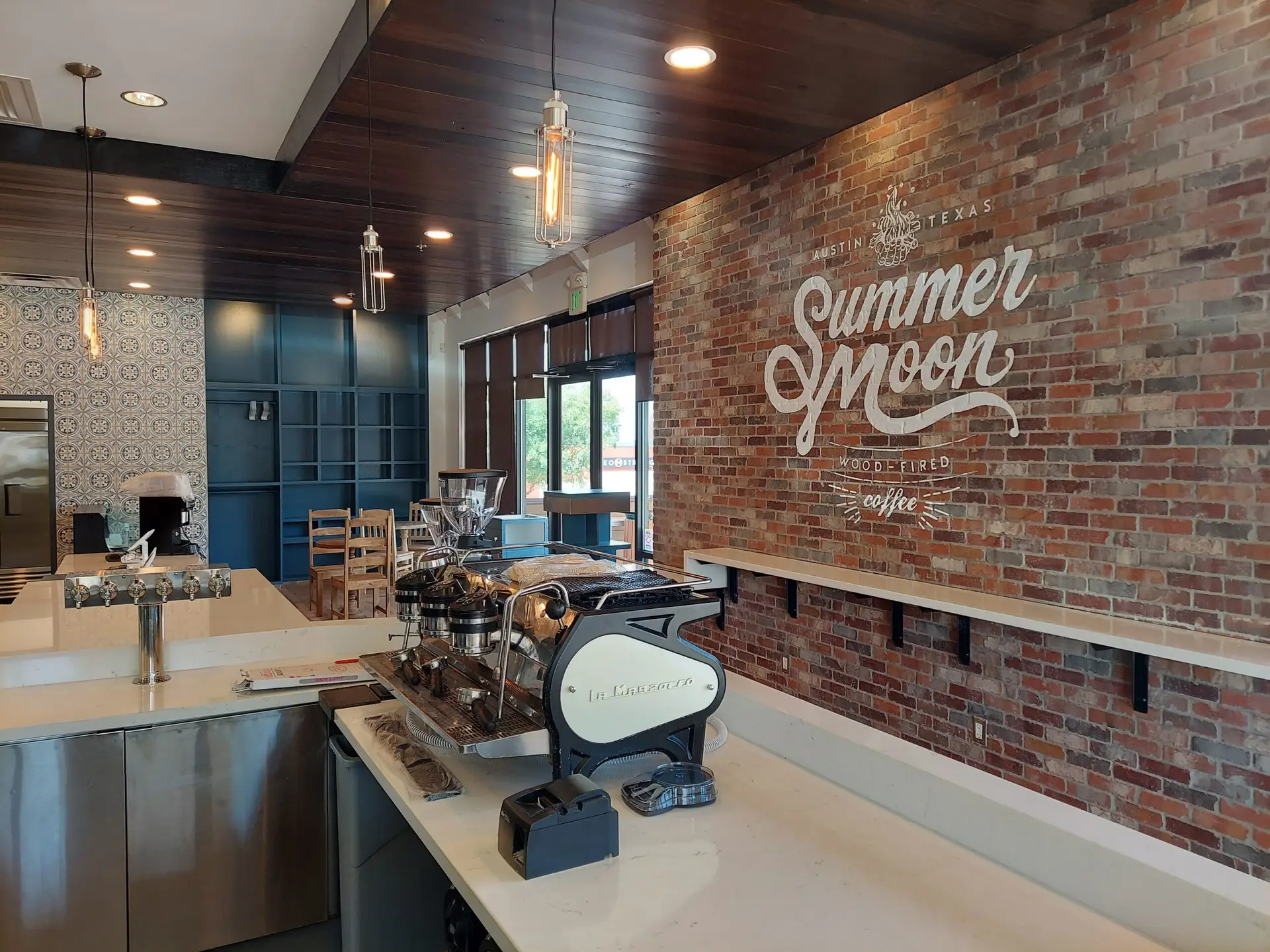 Espresso machine and service counter positioned in front of a brick wall with Summer Moon Coffee branding.